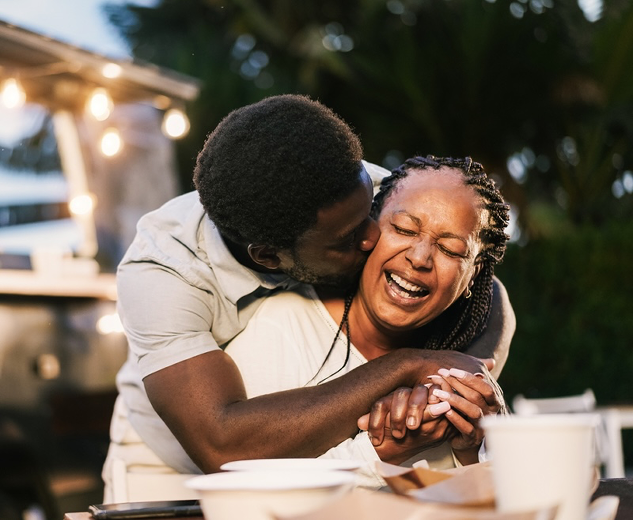 A son hugs his laughing mother and kisses her cheek